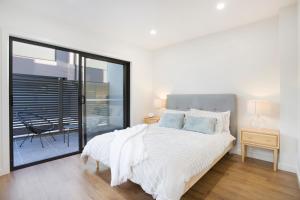 a white bedroom with a bed and a balcony at Stud Park Residence by Ready Set Stay in Rowville