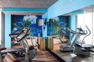 a gym with cardio machines and a palm tree mural at Novotel Suites München Parkstadt Schwabing in Munich