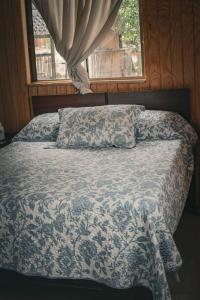 a bed with a blue and white comforter and a window at Cabaña Santa Amelia Antuco Pet Friendly in Peluca
