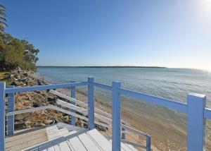 a blue railing next to a beach with the water at Burrum Beach House-Waterfront-Private Jetty-2BR in Toogoom +8 photos
