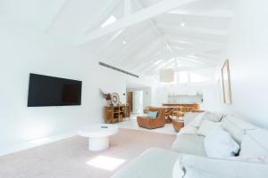 a white living room with a couch and a tv at La Casa Byron in Byron Bay