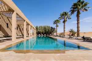 a swimming pool in a resort with palm trees at Kanz Erremal in Merzouga