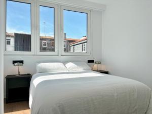 a white bed in a room with two windows at housingcoruña PLAZA DE ESPAÑA in A Coruña