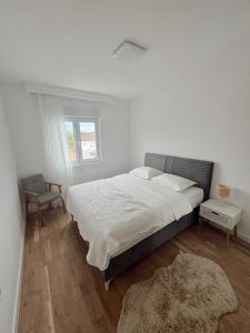 a white bedroom with a large bed and a chair at Apartman Barbara in Ljubuški