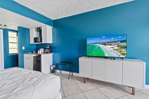 a bedroom with a bed and a tv on a blue wall at Oceanfront Inn, Private Balcony, 2 Full Beds #16 in Fort Pierce