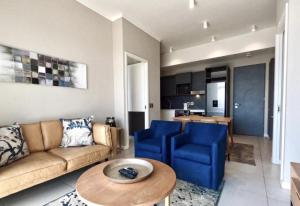 ein Wohnzimmer mit einer Couch und blauen Stühlen und einem Tisch in der Unterkunft Capital Trilogy Apartments in Pretoria