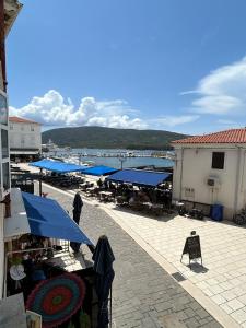a market with tables and blue umbrellas and a body of water at Apartman Lavanda in Cres