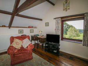 ein Wohnzimmer mit einem roten Sessel und einem Fernseher in der Unterkunft Beckaford Cottage in Newton Abbot