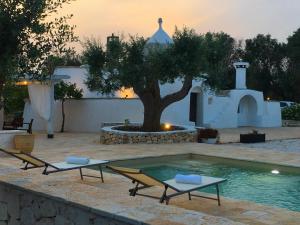 a swimming pool with two chairs and a tree at Trullo Tatauan in San Michele Salentino
