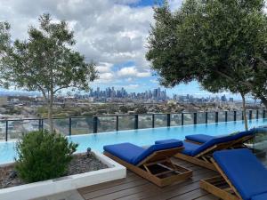 a swimming pool with two lounge chairs and a city skyline at FLEMINGTON - Melbourne City Views in Melbourne