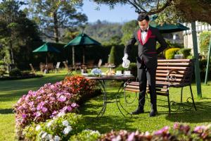 a man in a tuxedo standing next to a table in a park at The Hill Club in Nuwara Eliya