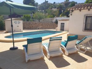 three chairs and an umbrella next to a swimming pool at Villa Casa Nuestra in Moraira