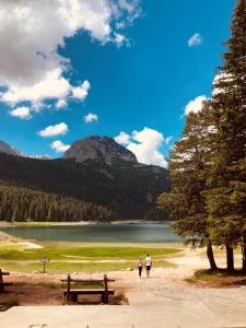 two people walking down a dirt path next to a lake at Lulu Cottage in Žabljak