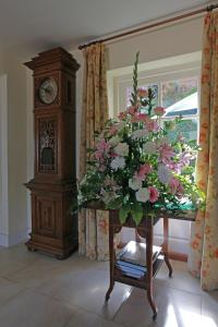 un reloj abuelo sentado junto a una mesa con flores en Ranvilles Farm House, en Romsey