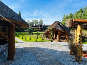 a building with a thatch roof and a house at Pod Kogutem i Sową - Bio Wioska z domkami Premium w góralskim stylu dla dorosłych in Postołowo