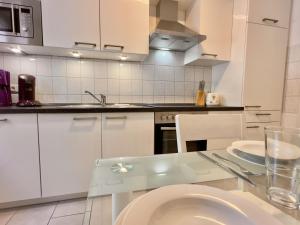 Una cocina con gabinetes blancos y una mesa de vidrio. en FeWo Küstenglück - Wilhelmshaven, en Wilhelmshaven 11 fotos más