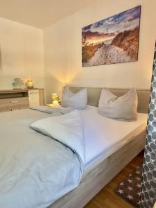 una habitación con una cama grande con sábanas y almohadas blancas en FeWo Küstenglück - Wilhelmshaven, en Wilhelmshaven