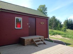 a red building with a bench on a deck at Lauku namiņš - Country cottage in Vecpiebalga