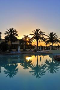 einen Pool mit Palmen und Sonnenuntergang im Hintergrund in der Unterkunft Argonauti Greenblu Resort in Marina di Pisticci