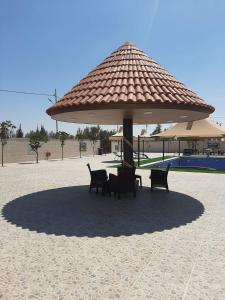 a table and chairs under a large umbrella on the beach at شاليهات ومسابح مزارع in Al Azraq ash Shamālī