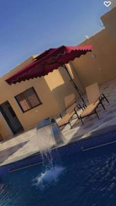 a pool with an umbrella and chairs next to a house at شاليهات ومسابح مزارع in Al Azraq ash Shamālī