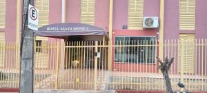 uma cerca em frente a um prédio rosa com um guarda-chuva em Hotel Sta Mônica Marília em Marília