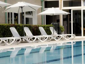 a row of white chairs and umbrellas next to a swimming pool at Hotel Arezzo ASC in Arezzo