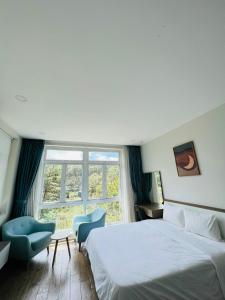 ein Schlafzimmer mit einem Bett und zwei Stühlen und einem Fenster in der Unterkunft Villa Hồ Tuyền Lâm Đà Lạt View Rừng Thông Đà Lạt in Xuan An