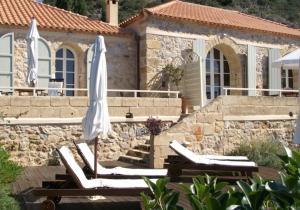 a couple of lounge chairs and an umbrella in front of a house at Katikies Manis in Kardamili