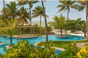 a large swimming pool with palm trees and the beach at Espelho Bahia Blue House in Praia do Espelho