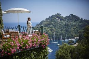 a woman standing on a balcony with an umbrella and flowers at Splendido, A Belmond Hotel, Portofino in Portofino