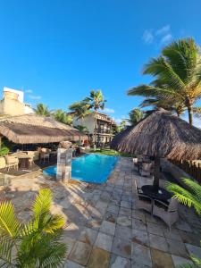 a resort with a swimming pool with a straw umbrella at Pousada Recanto do Lobo in Porto De Galinhas