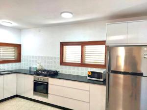 a kitchen with white cabinets and a stainless steel refrigerator at שלווה במושבה מגדל - וילה מדהימה עם בריכה פרטית וג'קוזי ליד הכנרת in Migdal