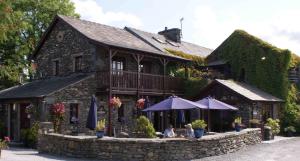 een gebouw waar twee mensen onder paraplu's voor zitten bij The Watermill Inn & Brewery in Windermere