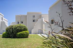 a white building with a hedge in front of it at Iris house Agios Sostis in Agios Sostis