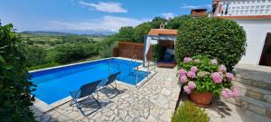 a swimming pool with two chairs and flowers next to a house at Rustic Apartment Mariva in Ljubač