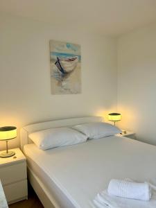 a white bed with two lamps and a painting on the wall at Apartman Ante Škoda Pivica in Povljana +23 photos