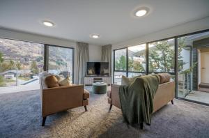 uma sala de estar com duas cadeiras e uma televisão e janelas em Redfern Retreat em Queenstown