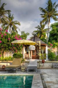a pool with two chairs and an umbrella next to a house at Les Villas Ottalia Gili Meno in Gili Meno