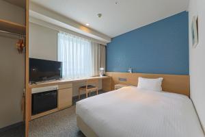 a bedroom with a bed and a desk with a television at JR Kyushu Hotel Miyazaki in Miyazaki