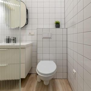 a white tiled bathroom with a toilet and a sink at Studio on Laisves Aleja, Central Kaunas - Self Check In in Kaunas
