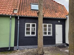 a black house with an orange roof and two windows at Skrædderens Baghus in Assens