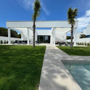 a white house with palm trees and a swimming pool at Poniente Beach House in Chiclana de la Frontera