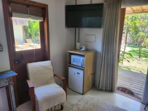 a living room with a tv and a chair and a window at Suíte Caju - Conforto e Exclusividade em Trancoso in Trancoso