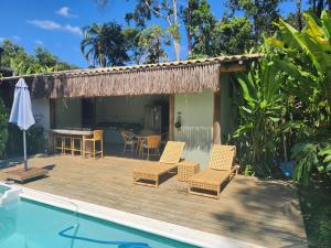 a deck with chairs and a table next to a pool at Suíte Caju - Conforto e Exclusividade em Trancoso in Trancoso