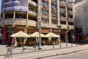 a building with tables and umbrellas on a city street at 20 Apartment Centre in Bucharest