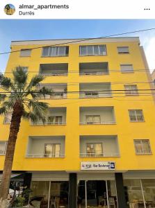a yellow building with a palm tree in front of it at Almar Apartments in Durrës