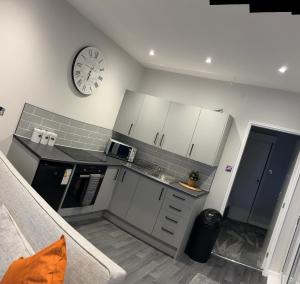 a kitchen with white cabinets and a clock on the wall at Goldie's Retreat in Blackrod +4 photos