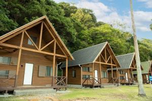 Un grupo de casas de troncos con árboles al fondo. en コテージ上浦, en Azamui