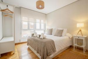 Un dormitorio con una cama con sábanas blancas y una ventana. en Apartamento Tres Mares, en Gijón